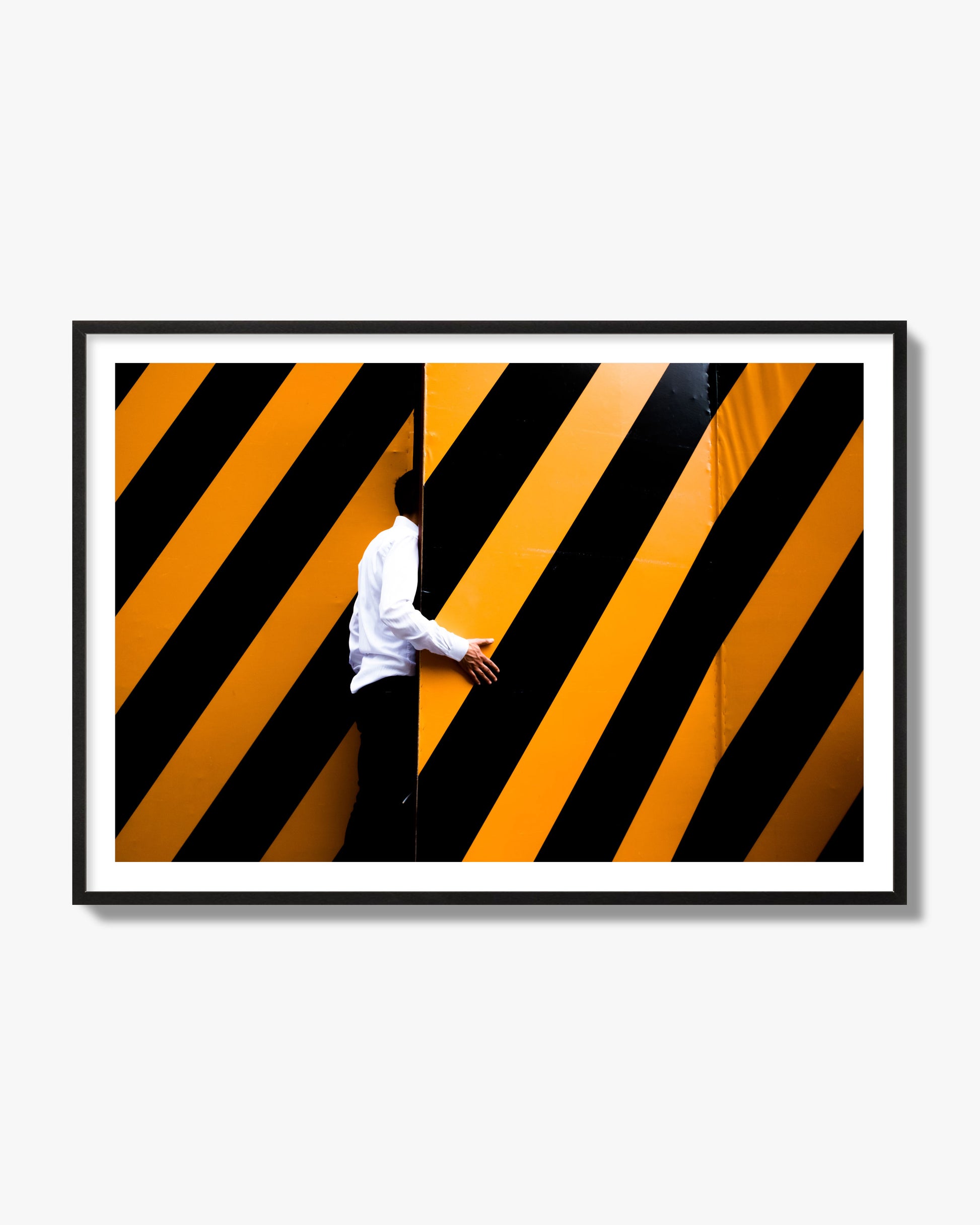Fine art street photograph of a man opening an orange and black stripped construction door. Archival pigment print, black frame.