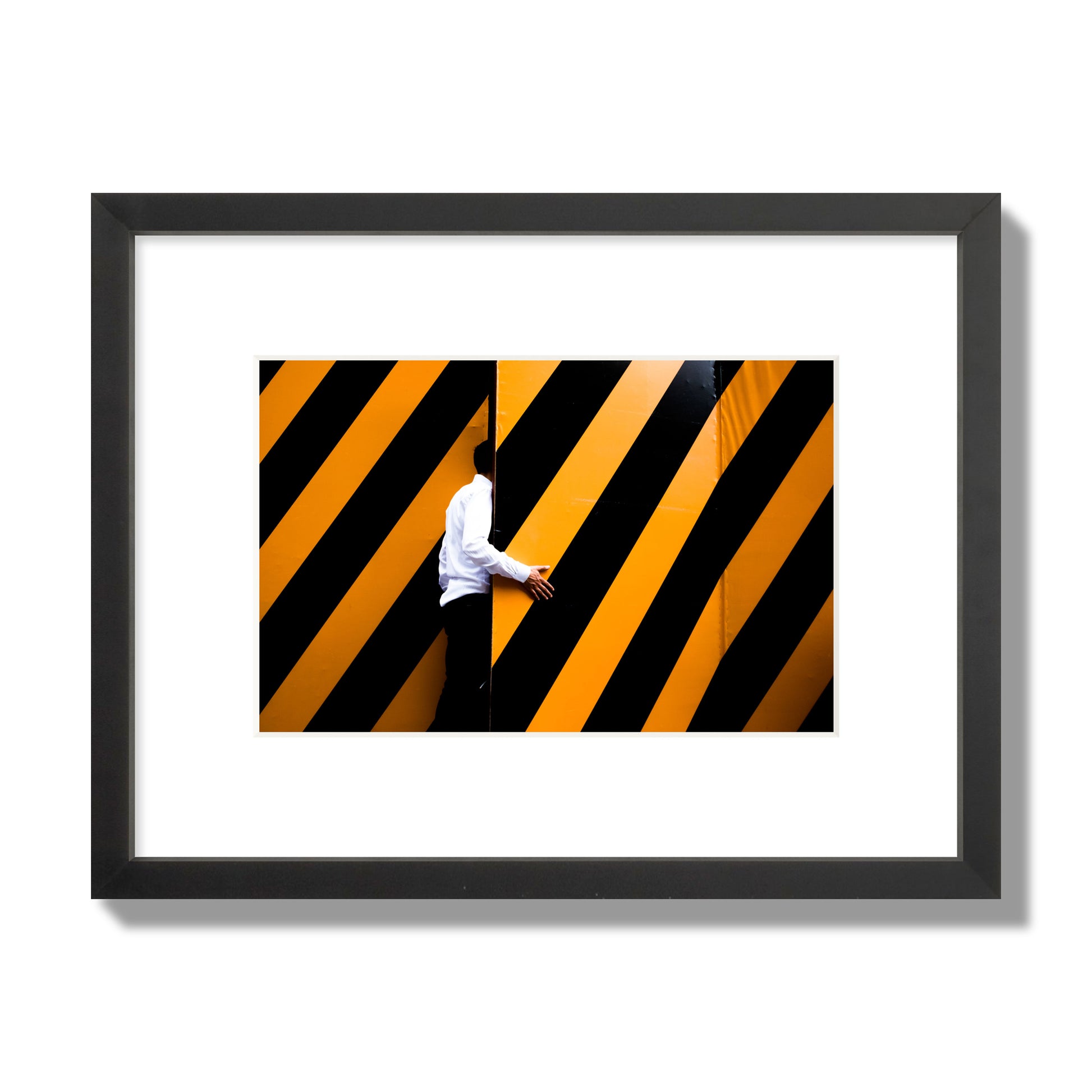 Fine art street photograph of a man opening an orange and black stripped construction door. Archival pigment print, small size, black frame.