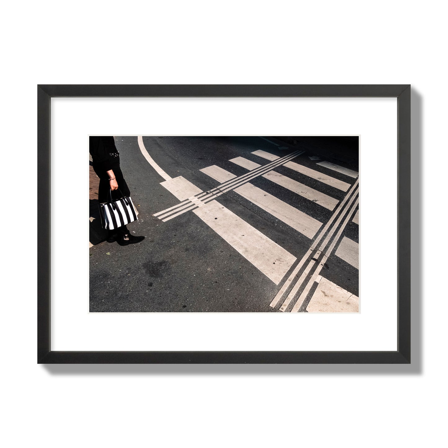 Fine art street photograph of a woman holding a black and white striped purse while crossing a black and white crosswalk. Archival pigment print, medium size, black frame.