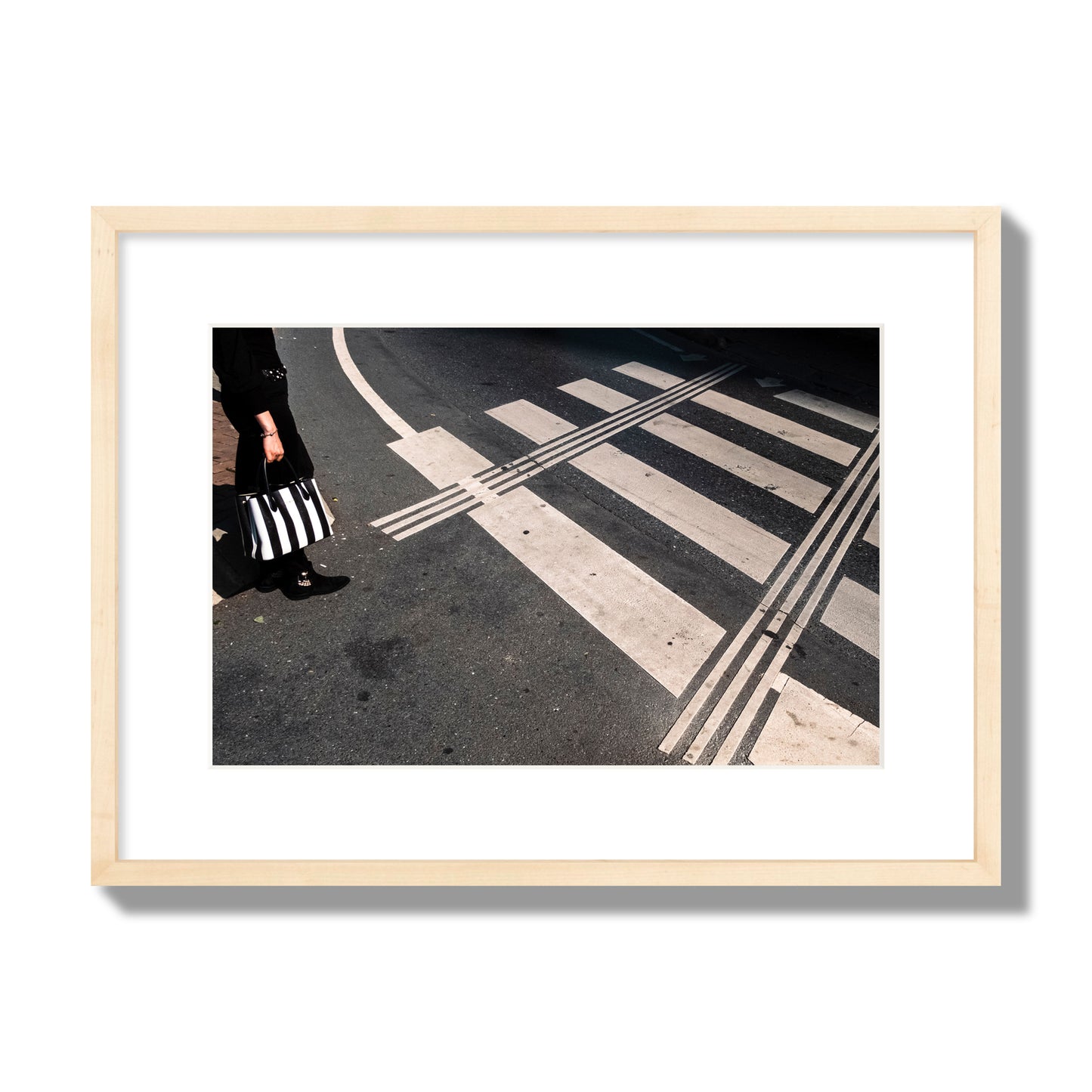 Fine art street photograph of a woman holding a black and white striped purse while crossing a black and white crosswalk. Archival pigment print, medium size, natural wood frame.
