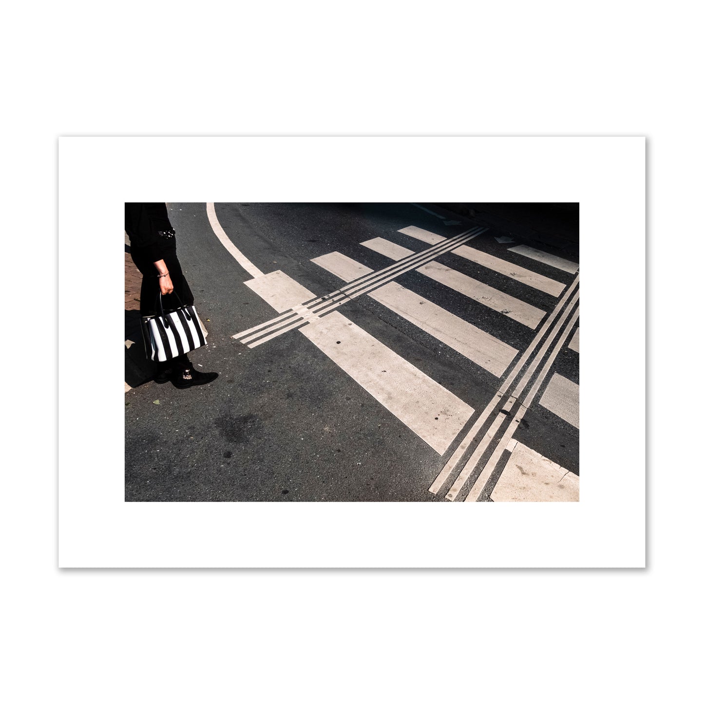 Fine art street photograph of a woman holding a black and white striped purse while crossing a black and white crosswalk. Archival pigment print, medium size, unframed.