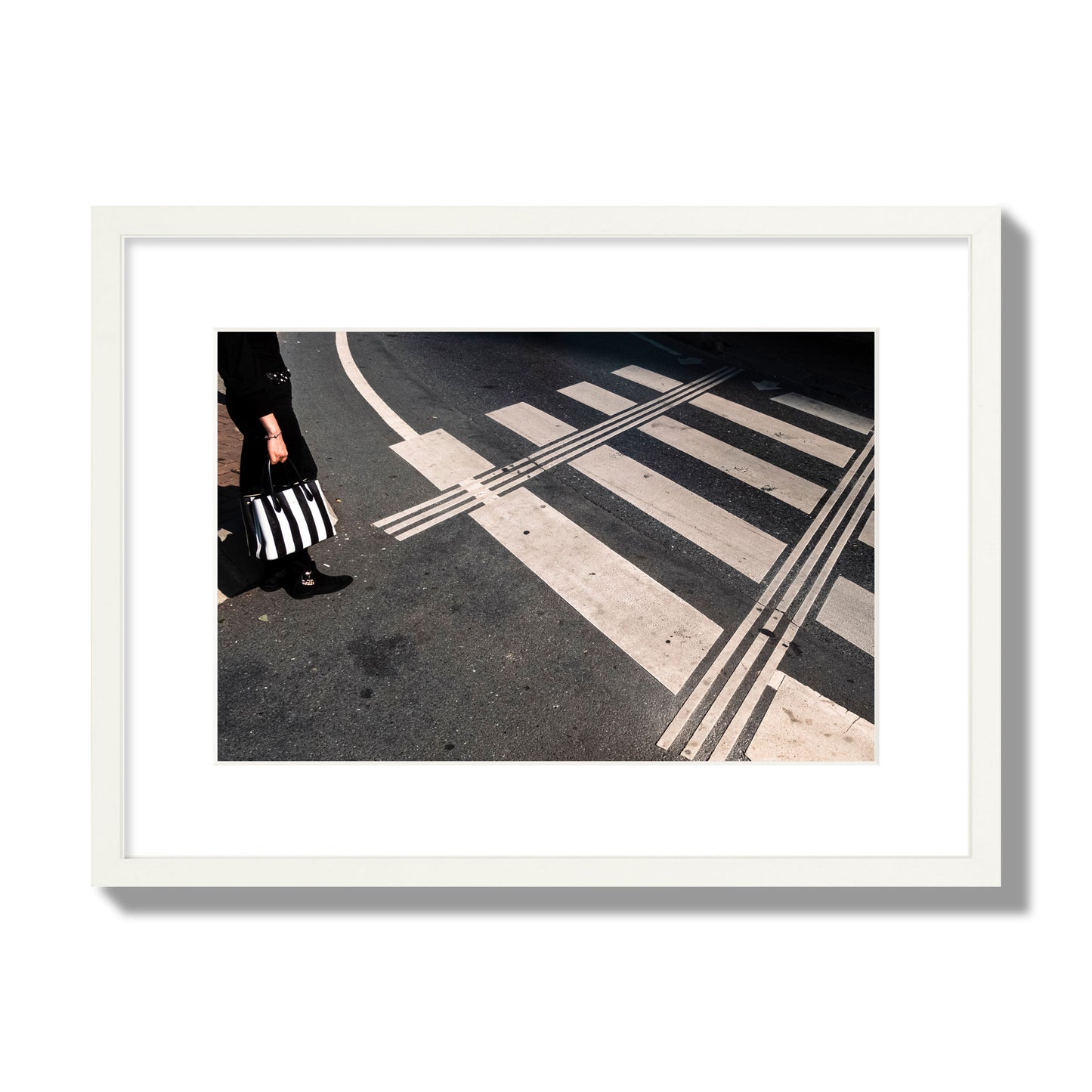 Fine art street photograph of a woman holding a black and white striped purse while crossing a black and white crosswalk. Archival pigment print, medium size, white frame.