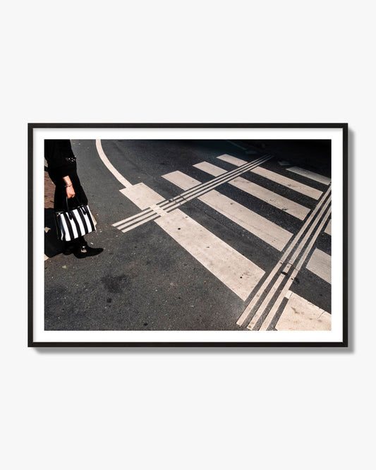 Fine art street photograph of a woman holding a black and white striped purse while crossing a black and white crosswalk. Archival pigment print, black frame.