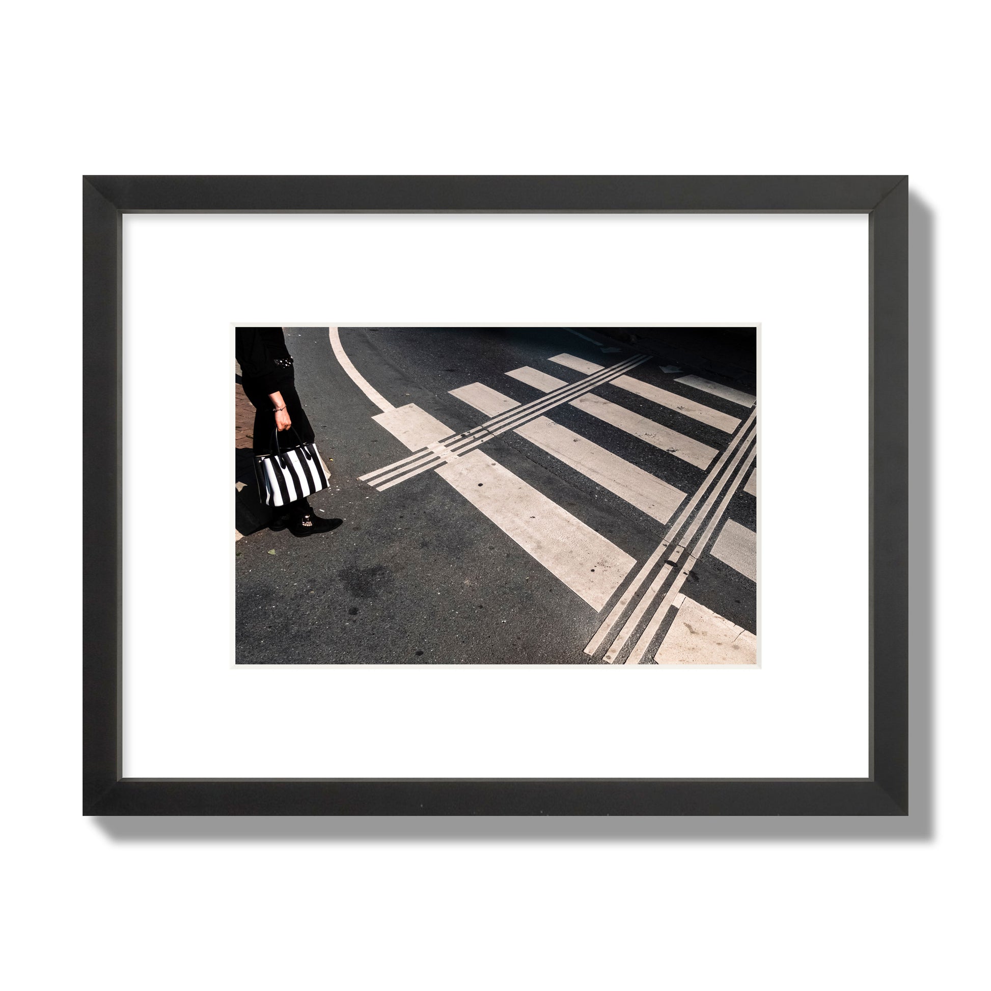 Fine art street photograph of a woman holding a black and white striped purse while crossing a black and white crosswalk. Archival pigment print, small size, black frame.