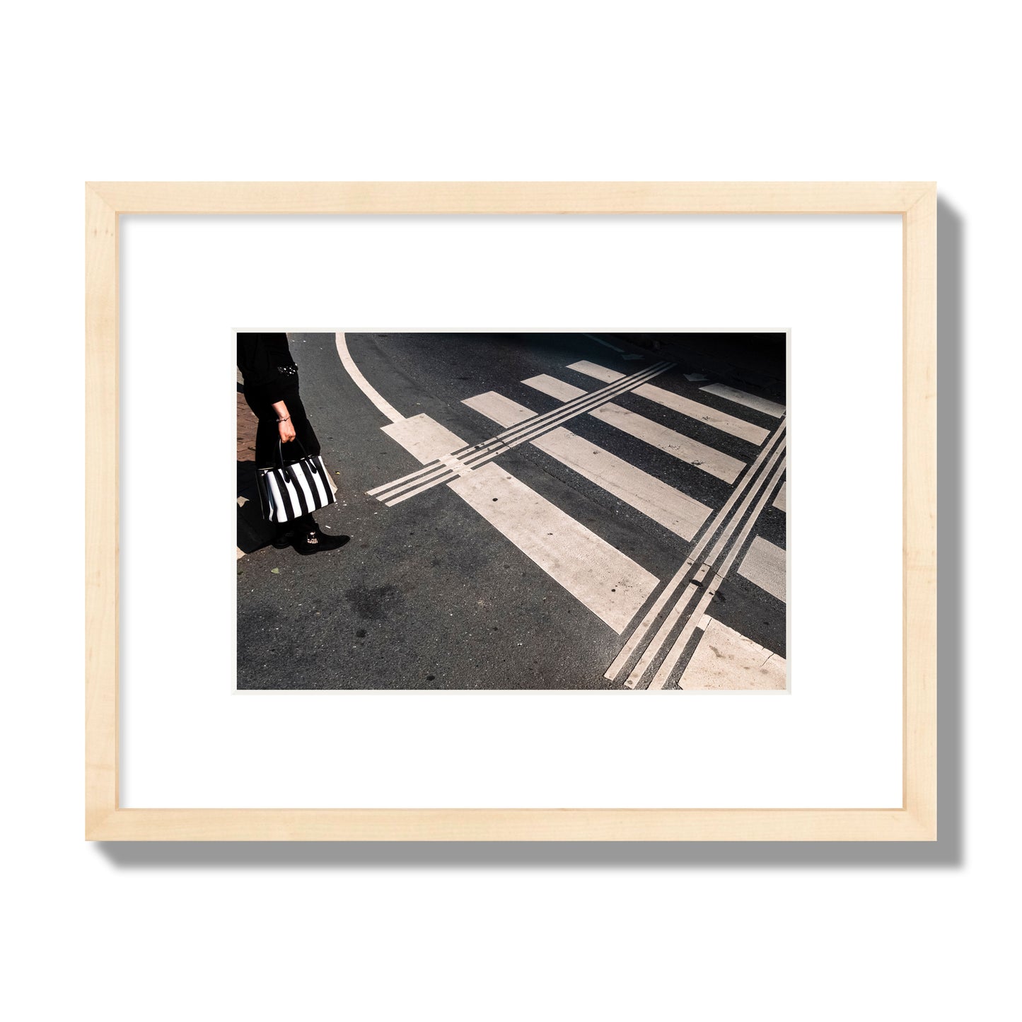 Fine art street photograph of a woman holding a black and white striped purse while crossing a black and white crosswalk. Archival pigment print, small size, natural wood frame.