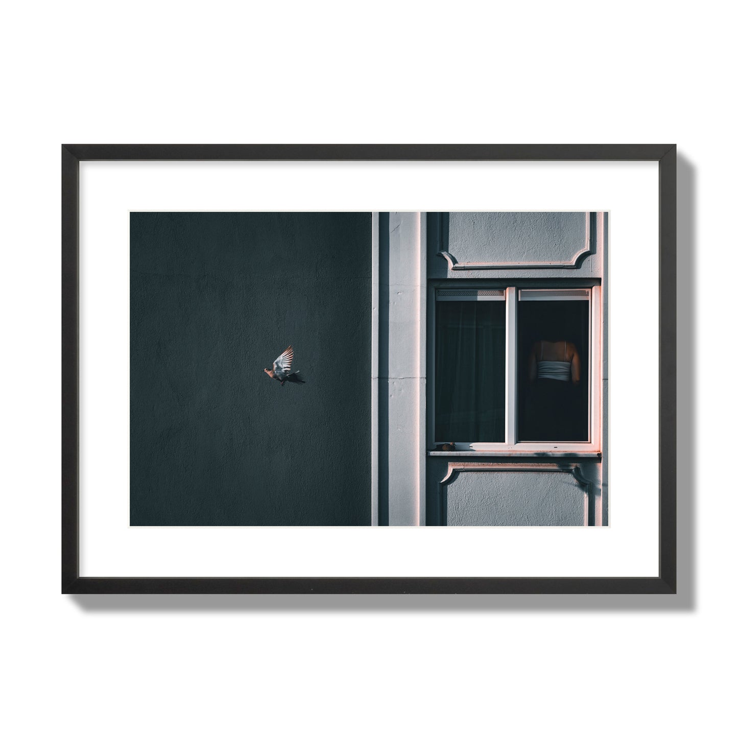 Fine art street photograph of a woman highlighted in a window on the right side of the frame, while a bird flies out of frame on the left. Archival pigment print, large size, black frame.