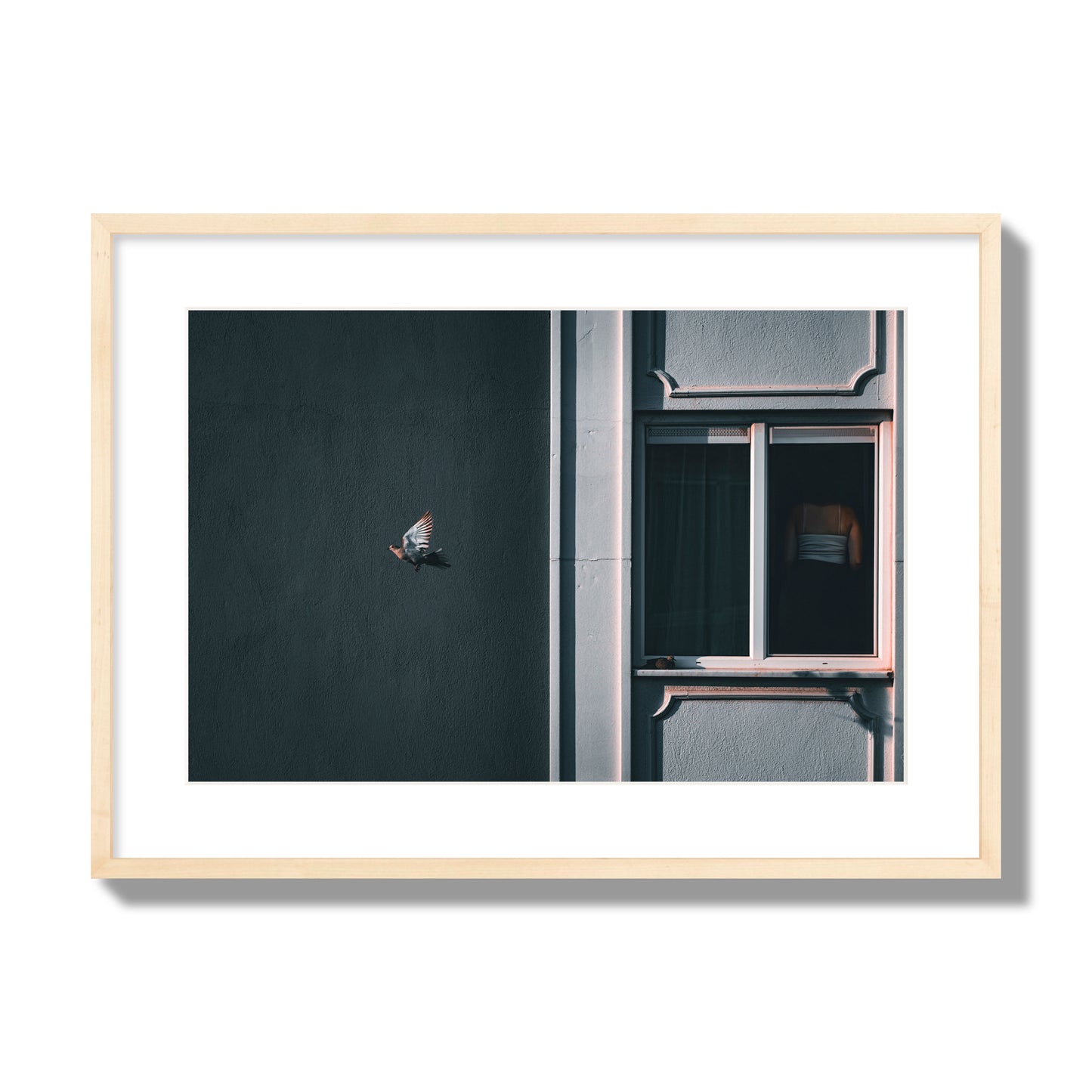 Fine art street photograph of a woman highlighted in a window on the right side of the frame, while a bird flies out of frame on the left. Archival pigment print, large size, natural wood frame.