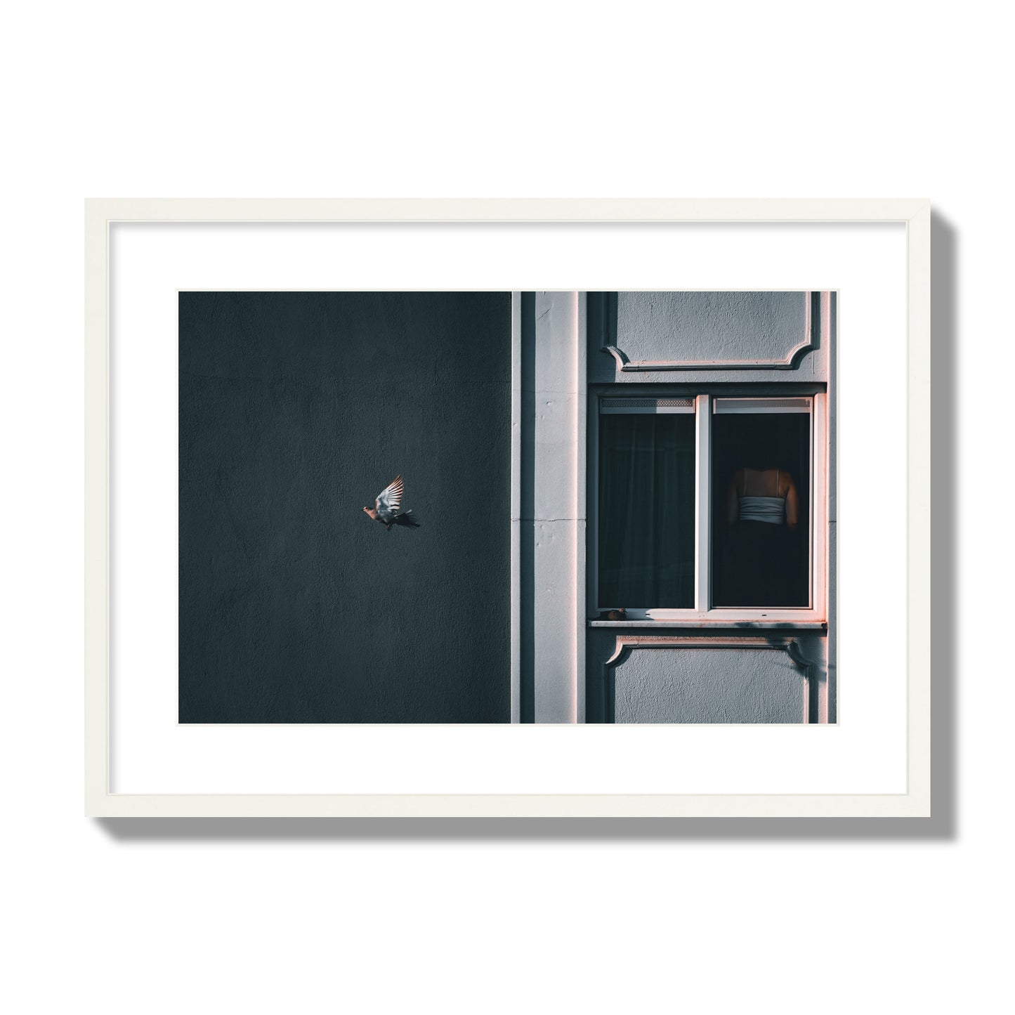 Fine art street photograph of a woman highlighted in a window on the right side of the frame, while a bird flies out of frame on the left. Archival pigment print, large size, white frame.