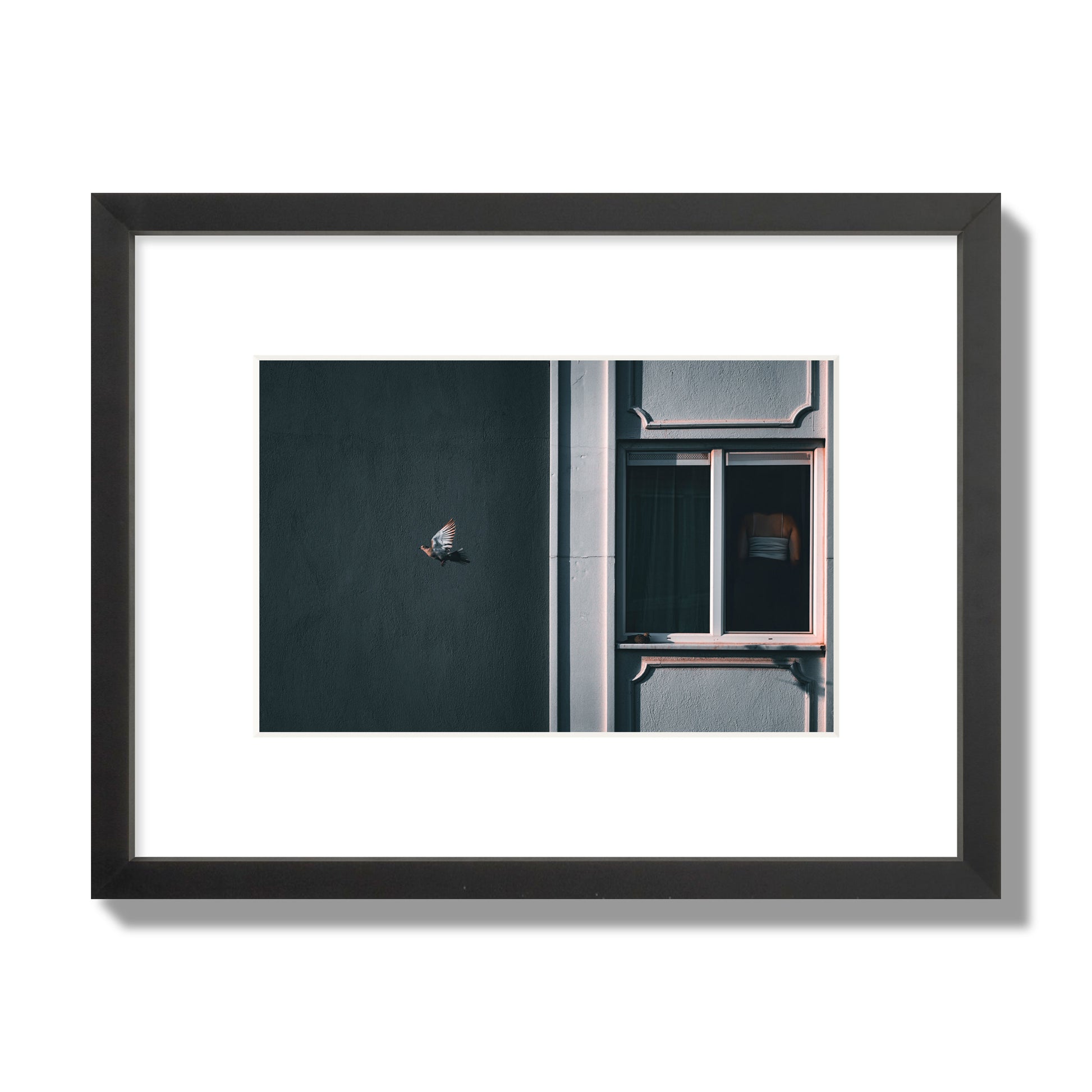 Fine art street photograph of a woman highlighted in a window on the right side of the frame, while a bird flies out of frame on the left. Archival pigment print, small size, black frame.