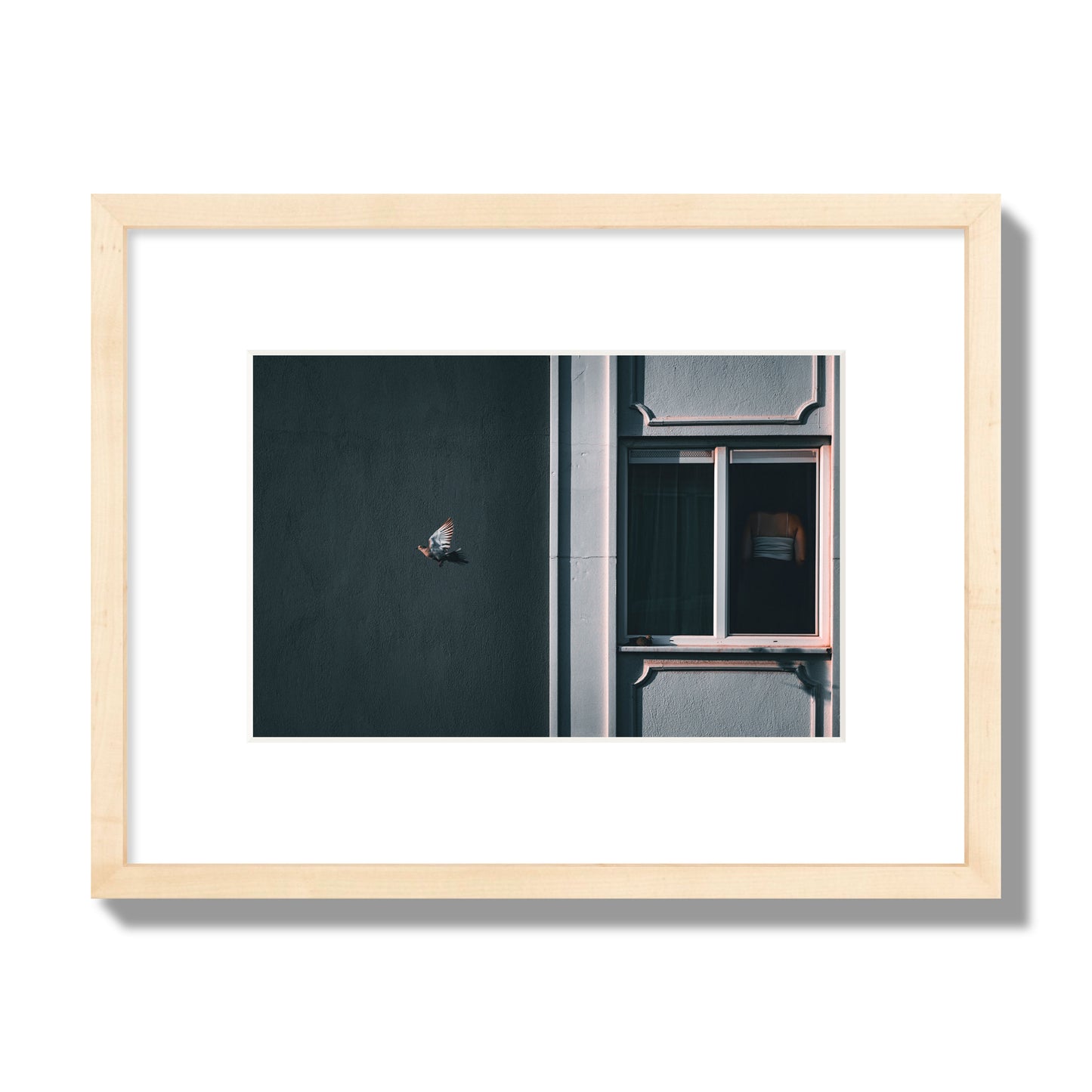 Fine art street photograph of a woman highlighted in a window on the right side of the frame, while a bird flies out of frame on the left. Archival pigment print, small size, natural wood frame.