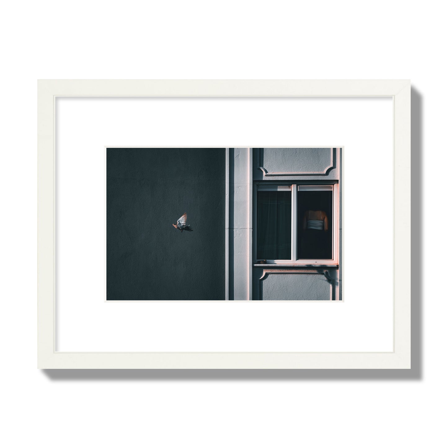 Fine art street photograph of a woman highlighted in a window on the right side of the frame, while a bird flies out of frame on the left. Archival pigment print, small size, white frame.