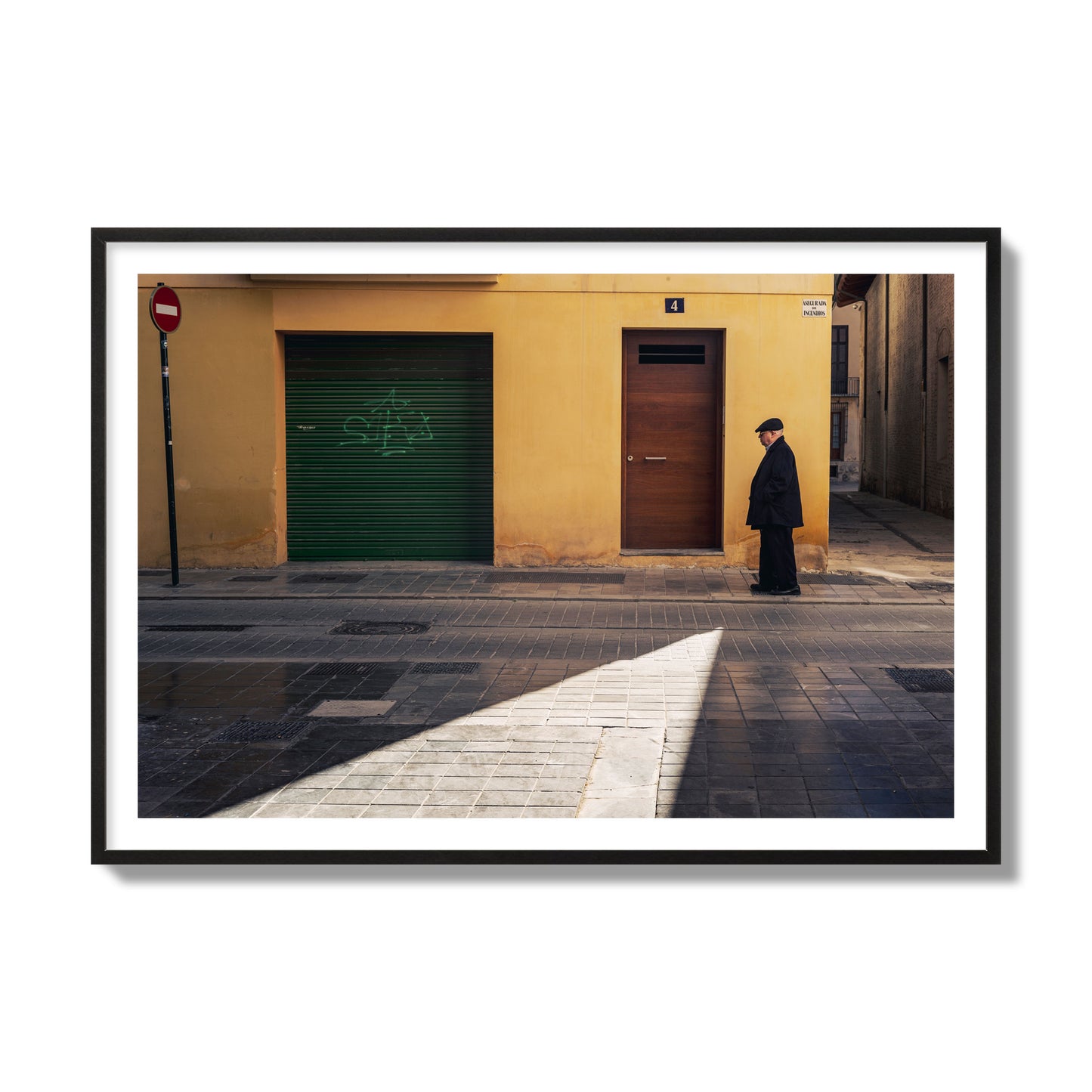 Fine art street photograph of an elderly man walking down a Valencia, Spain street with yellow and green walls, illuminated by a shaft of light. Archival pigment print, collector size, black frame.