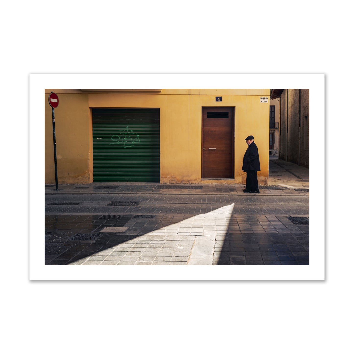 Fine art street photograph of an elderly man walking down a Valencia, Spain street with yellow and green walls, illuminated by a shaft of light. Archival pigment print, collector size, unframed.