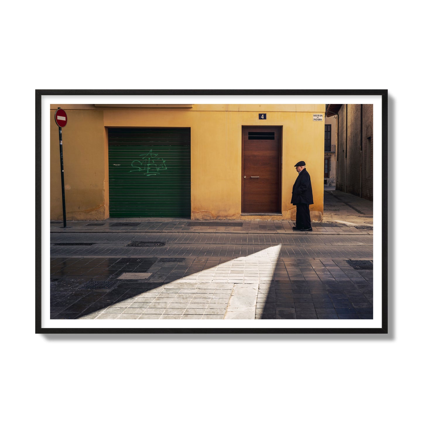 Fine art street photograph of an elderly man walking down a Valencia, Spain street with yellow and green walls, illuminated by a shaft of light. Archival pigment print, gallery size, black frame.
