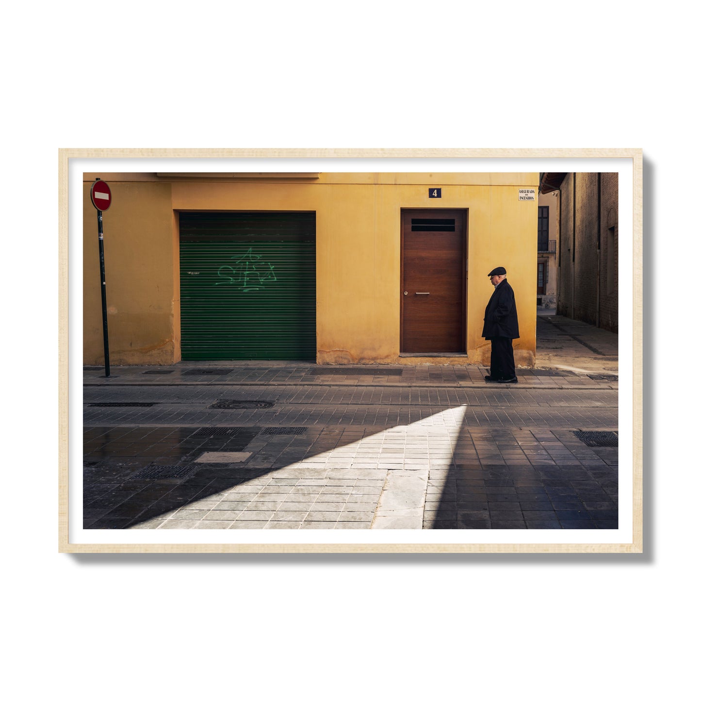 Fine art street photograph of an elderly man walking down a Valencia, Spain street with yellow and green walls, illuminated by a shaft of light. Archival pigment print, gallery size, natural wood frame.