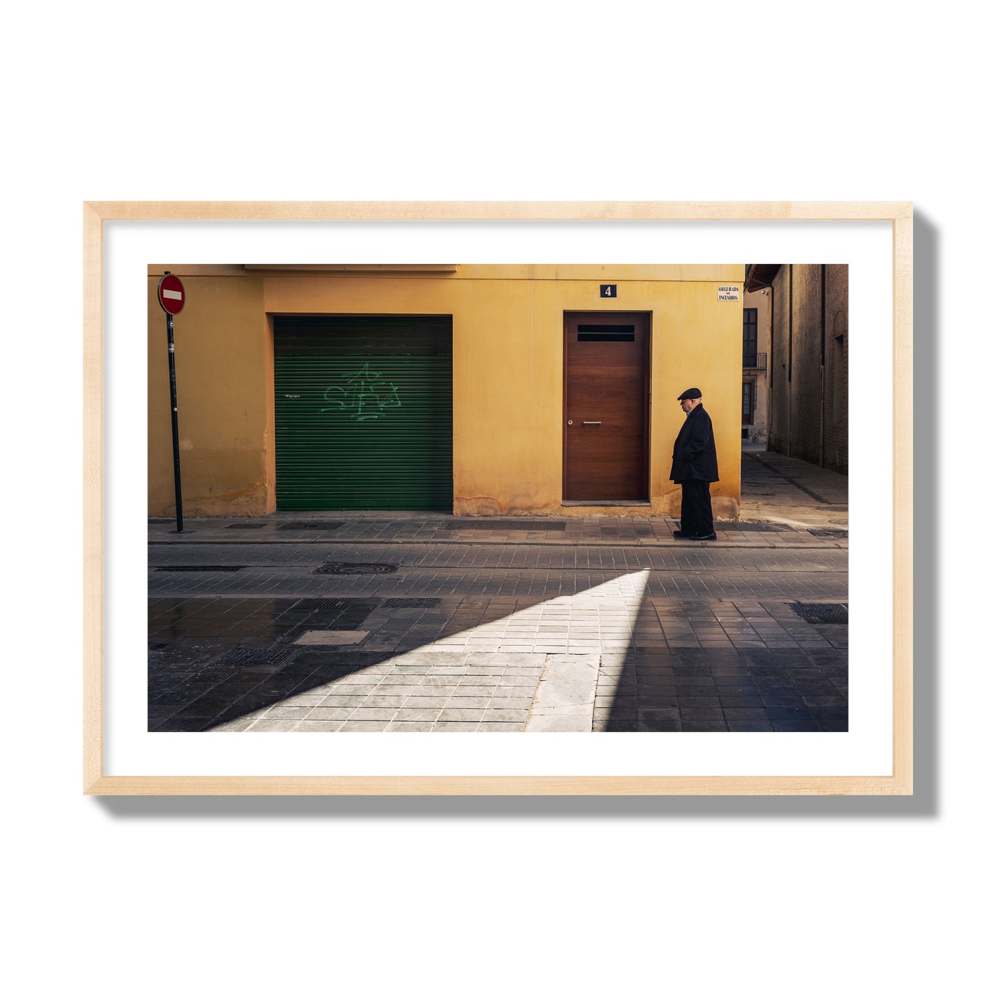 Fine art street photograph of an elderly man walking down a Valencia, Spain street with yellow and green walls, illuminated by a shaft of light. Archival pigment print, giant size, natural wood frame.