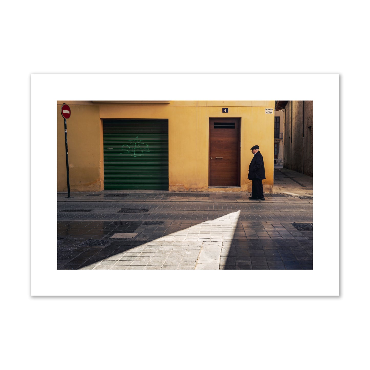 Fine art street photograph of an elderly man walking down a Valencia, Spain street with yellow and green walls, illuminated by a shaft of light. Archival pigment print, giant size, unframed.