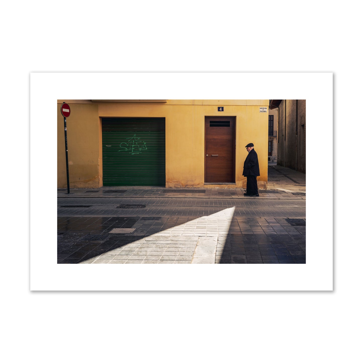 Fine art street photograph of an elderly man walking down a Valencia, Spain street with yellow and green walls, illuminated by a shaft of light. Archival pigment print, large size, unframed.