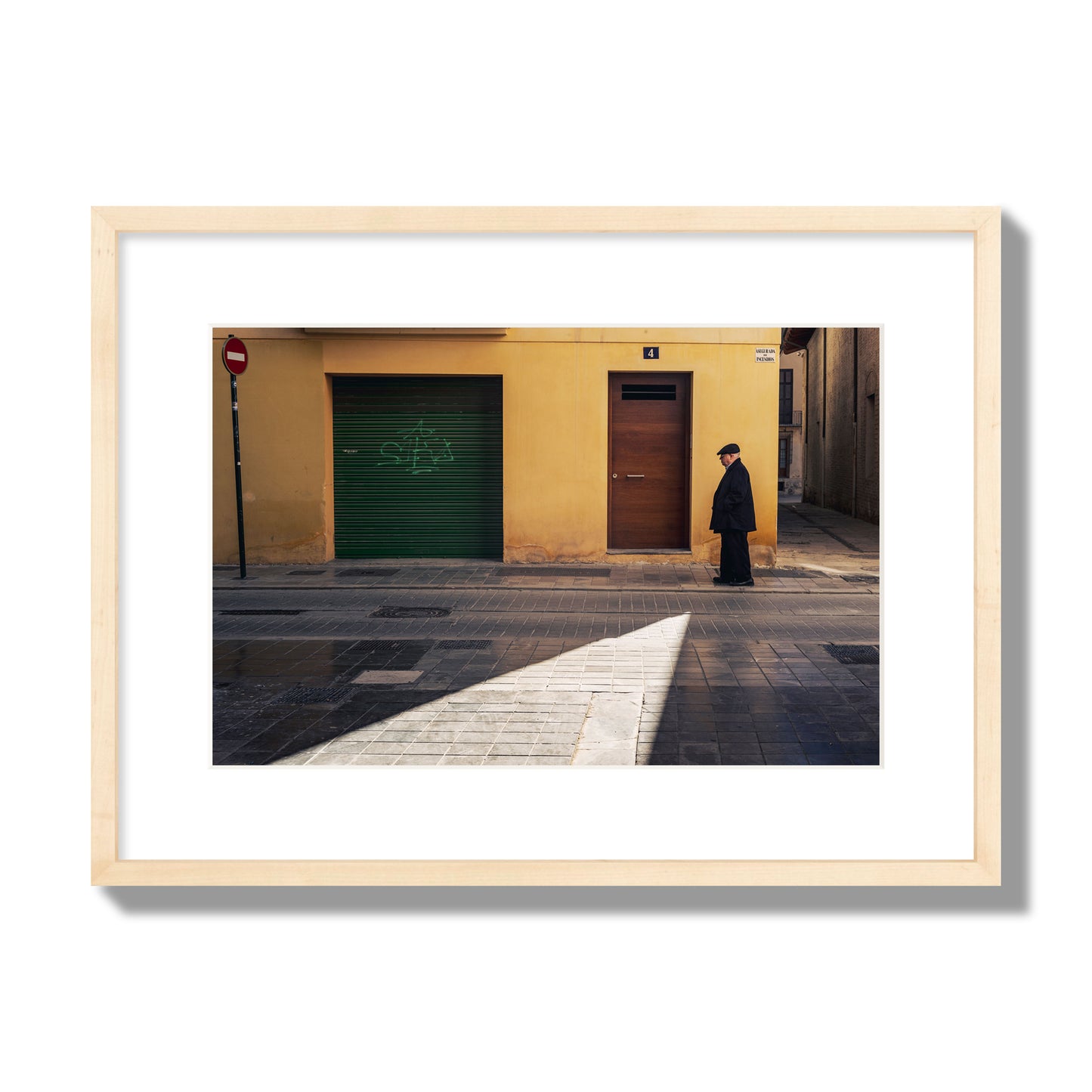 Fine art street photograph of an elderly man walking down a Valencia, Spain street with yellow and green walls, illuminated by a shaft of light. Archival pigment print, medium size, natural wood frame.