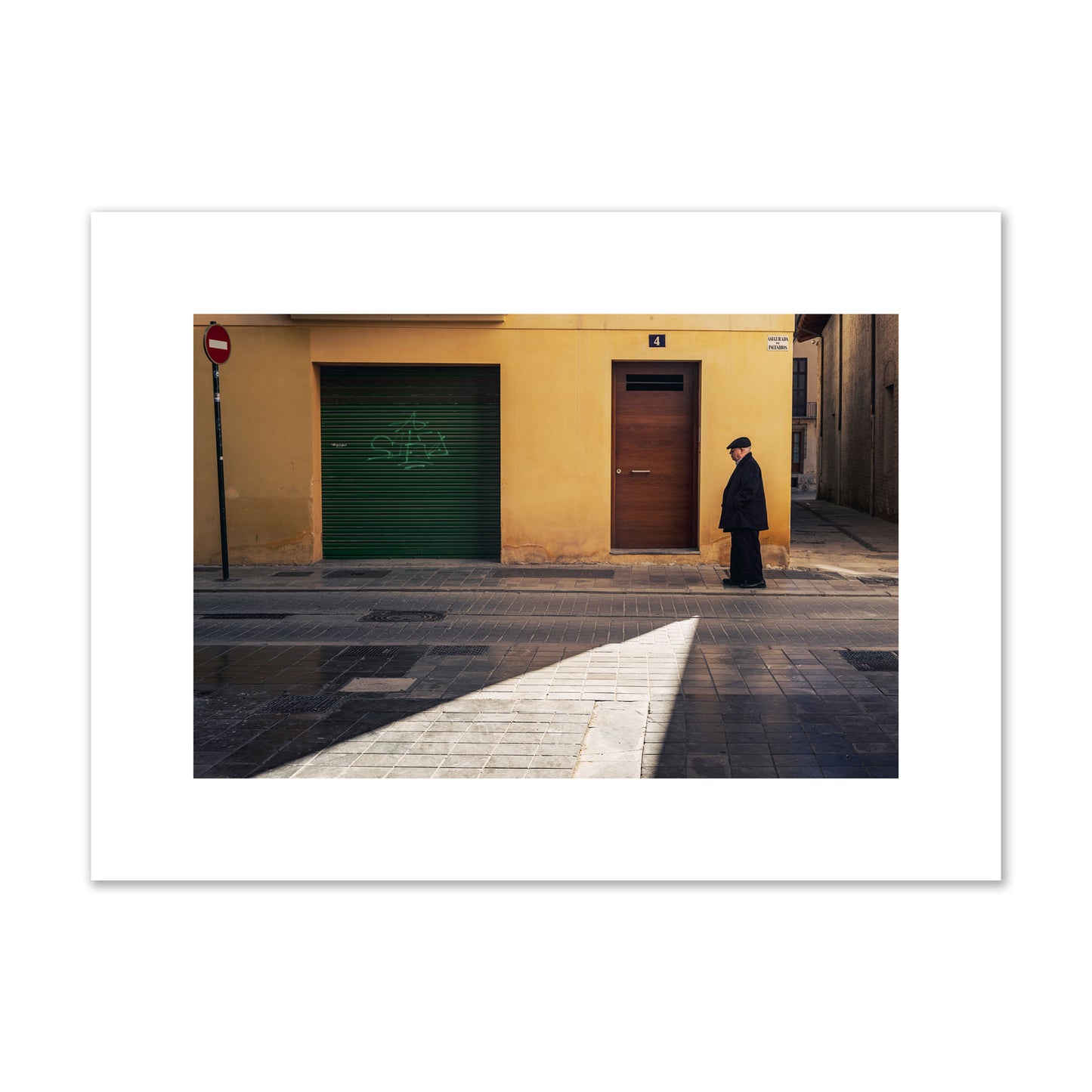 Fine art street photograph of an elderly man walking down a Valencia, Spain street with yellow and green walls, illuminated by a shaft of light. Archival pigment print, medium size, unframed.