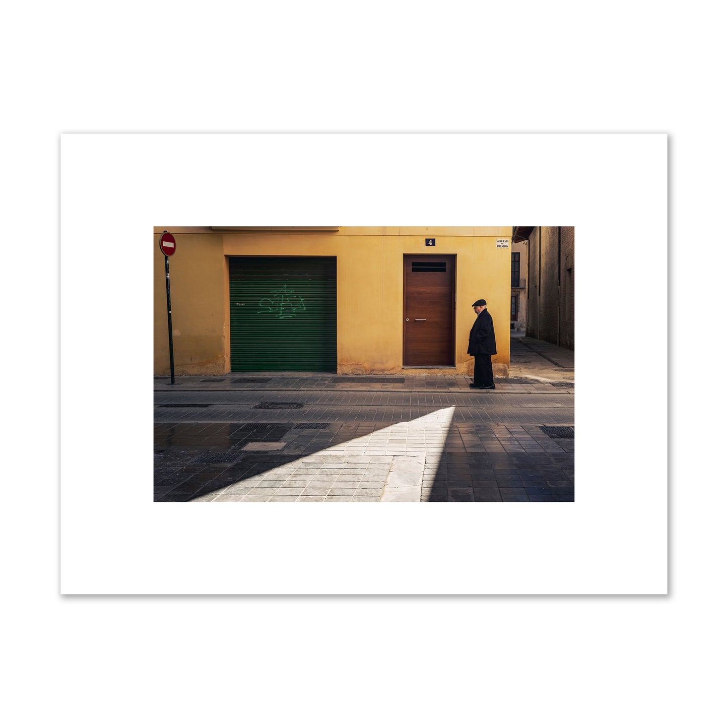 Fine art street photograph of an elderly man walking down a Valencia, Spain street with yellow and green walls, illuminated by a shaft of light. Archival pigment print, small size, unframed.