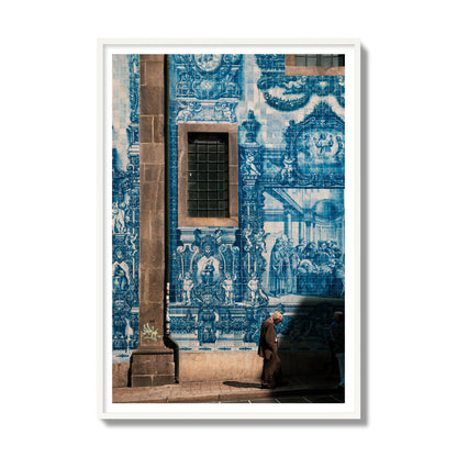 Fine art street photograph of an elderly man walking past traditional blue azulejo tile mural on a historic building in Lisbon, Portugal, archival pigment print, gallery size, white frame.
