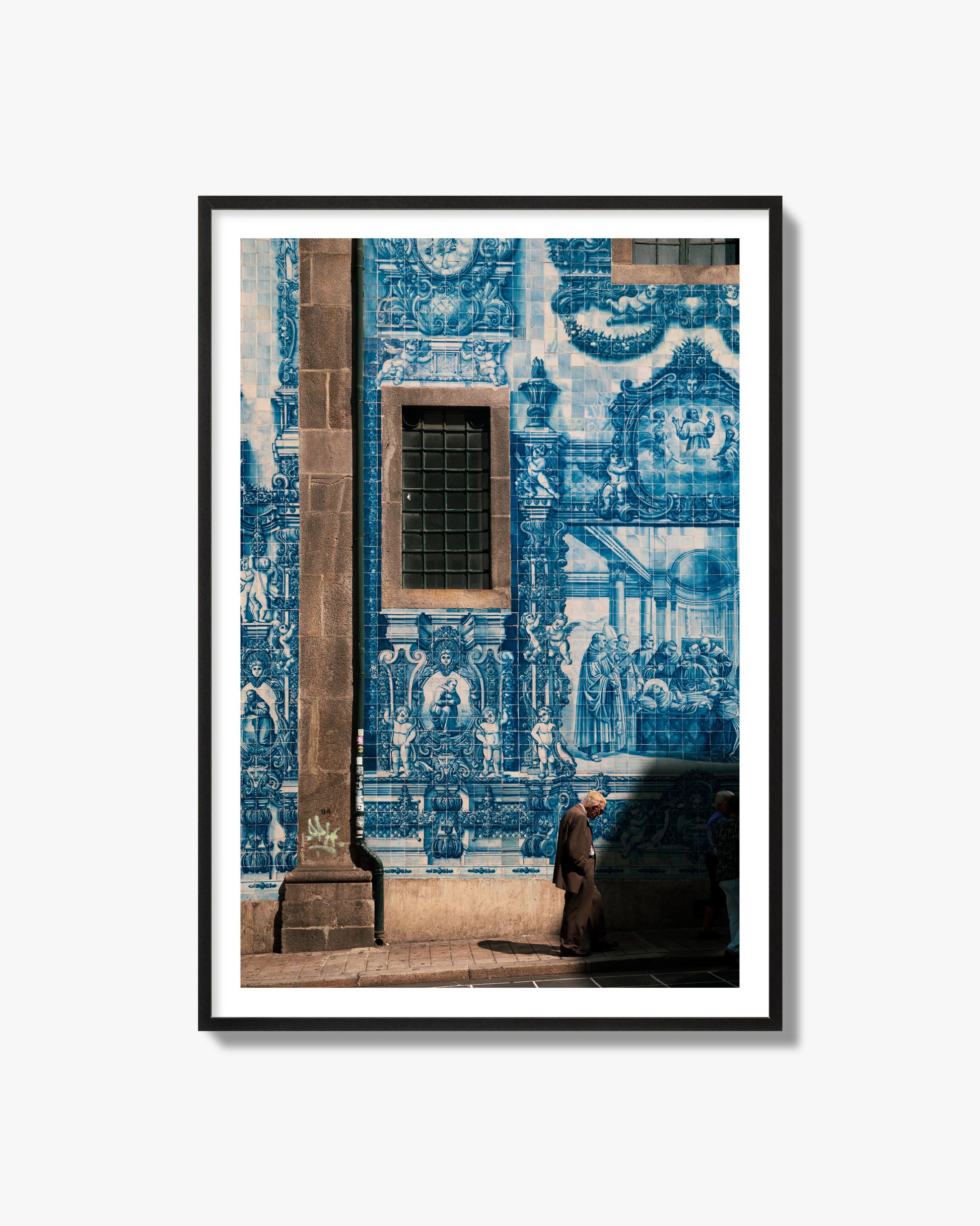 Fine art street photograph of an elderly man walking past traditional blue azulejo tile mural on a historic building in Lisbon, Portugal, archival pigment print, black frame.