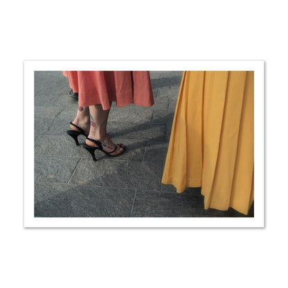 Fine art candid street photo of women in coral and mustard skirts with black heels, featuring a tattooed ankle that reads “much better”. Archival pigment print, gallery size, print.