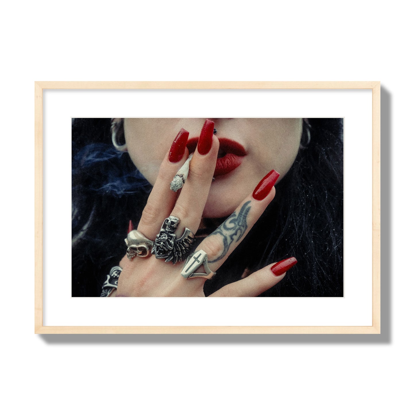 Fine art close-up photograph of a woman smoking, her hands covered with chunky rings and tattoos. Archival pigment print, large size, natural wood frame.