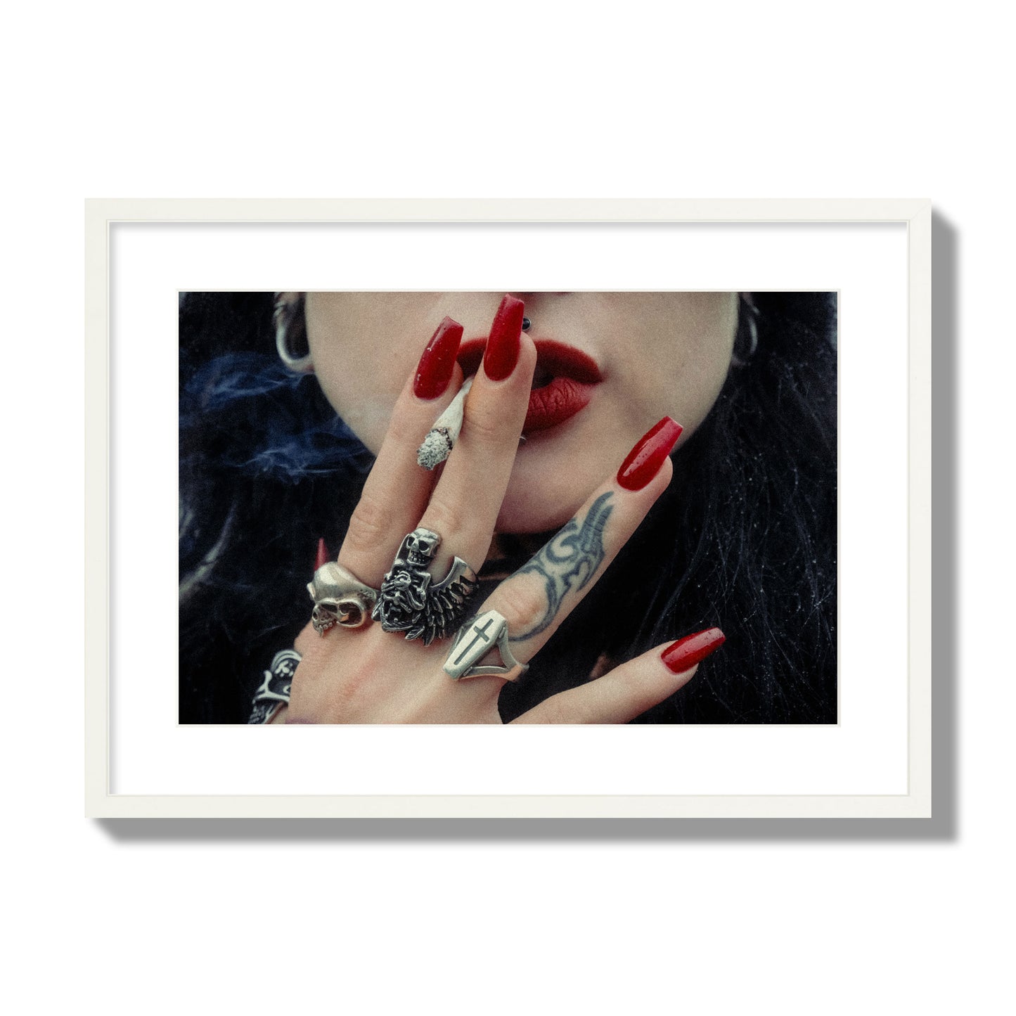Fine art close-up photograph of a woman smoking, her hands covered with chunky rings and tattoos. Archival pigment print, large size, white frame.