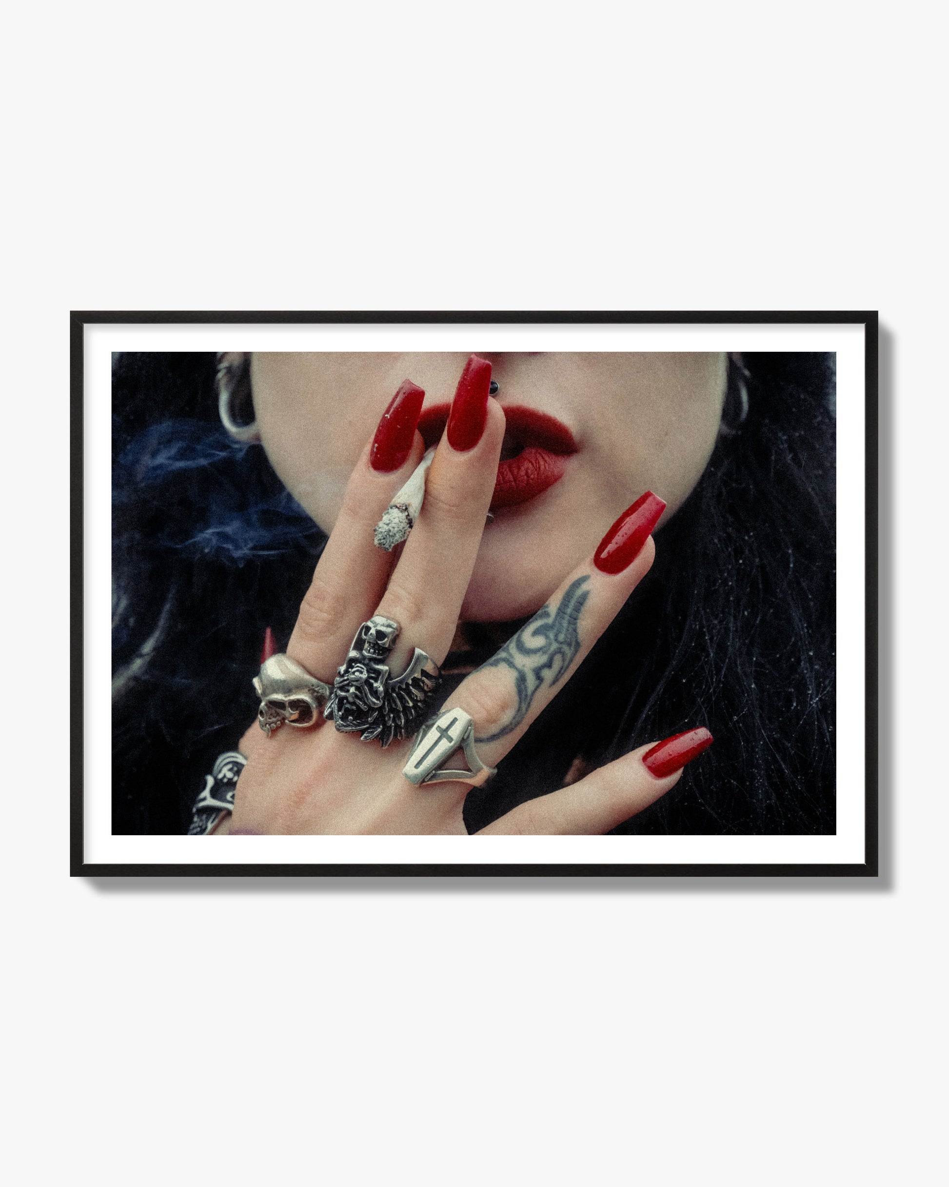 Fine art close-up photograph of a woman smoking, her hands covered with chunky rings and tattoos. Archival pigment print, black frame.