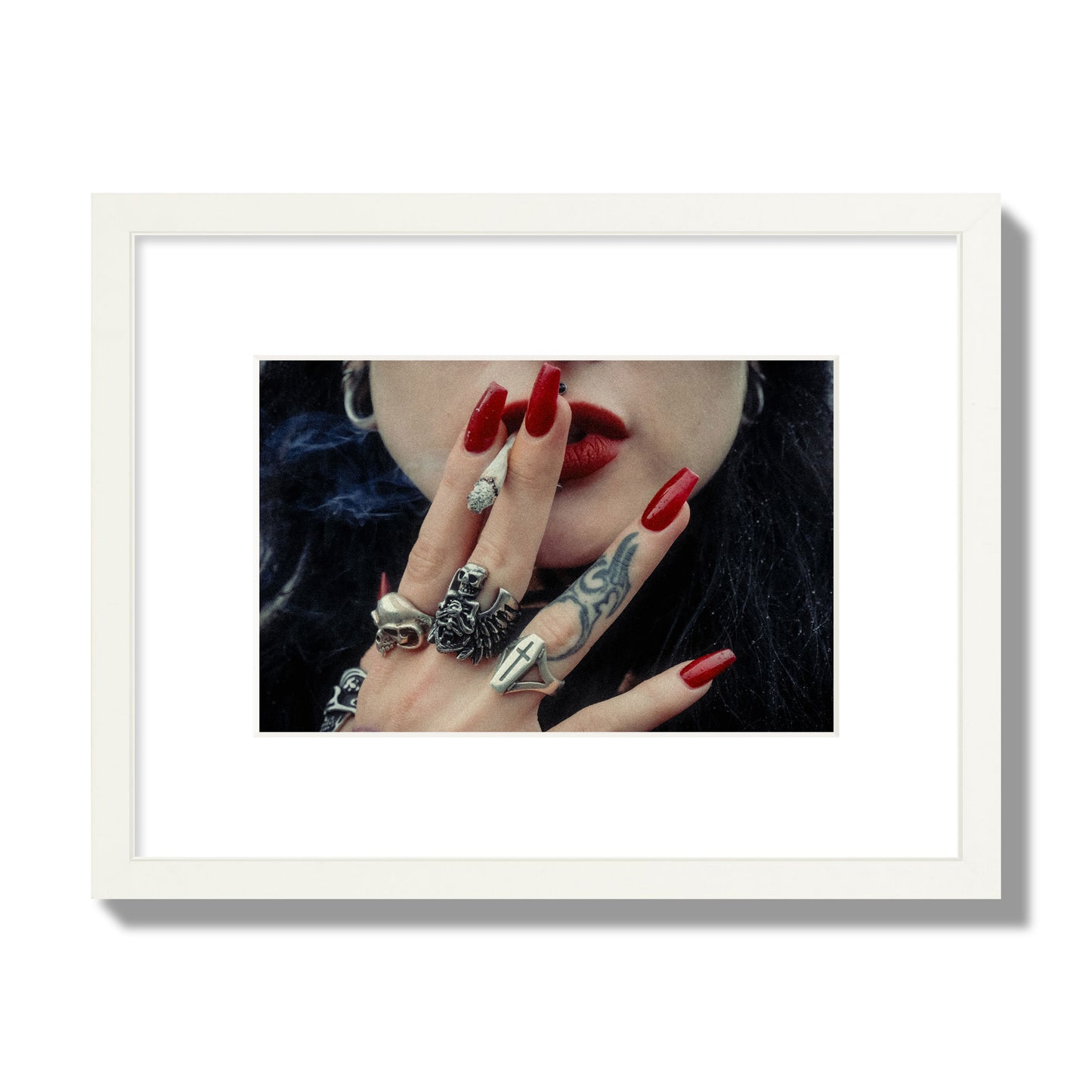Fine art close-up photograph of a woman smoking, her hands covered with chunky rings and tattoos. Archival pigment print, small size, white frame.