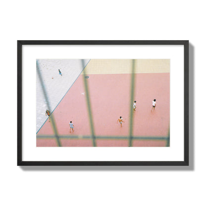 Fine art street photograph of a geometric outdoor scene in Portugal with people playing soccer on a pink field, archival pigment print, large size, black frame.