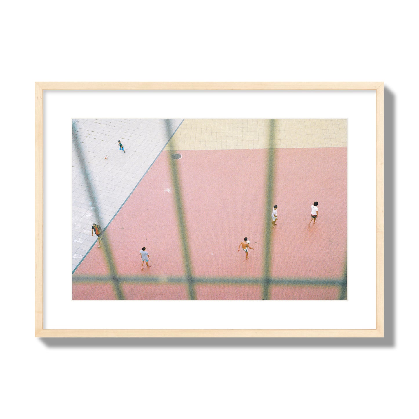 Fine art street photograph of a geometric outdoor scene in Portugal with people playing soccer on a pink field, archival pigment print, large size, natural wood frame.