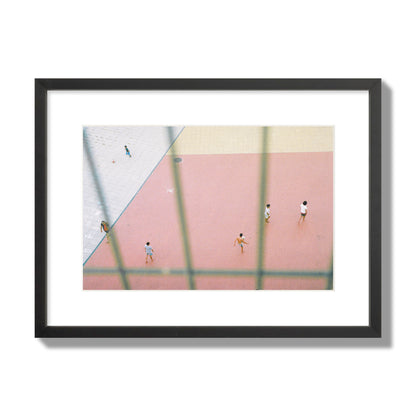 Fine art street photograph of a geometric outdoor scene in Portugal with people playing soccer on a pink field, archival pigment print, medium size, black frame.