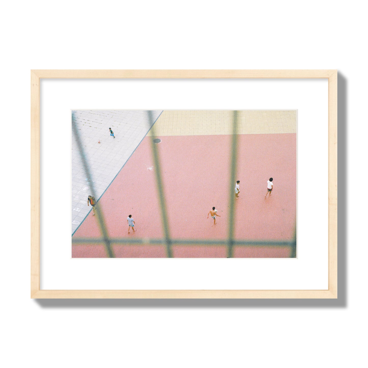 Fine art street photograph of a geometric outdoor scene in Portugal with people playing soccer on a pink field, archival pigment print, medium size, natural wood frame.