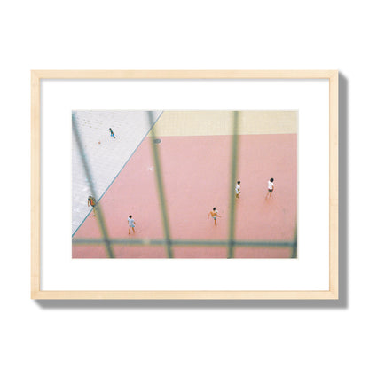 Fine art street photograph of a geometric outdoor scene in Portugal with people playing soccer on a pink field, archival pigment print, medium size, natural wood frame.
