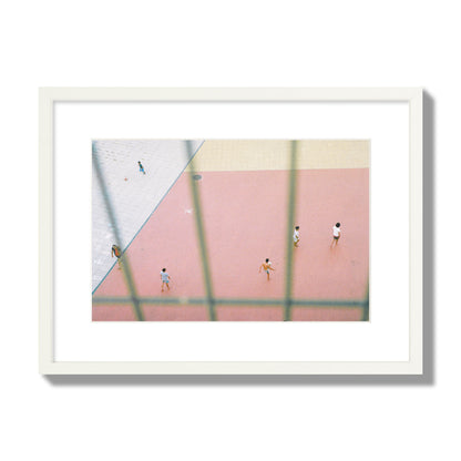 Fine art street photograph of a geometric outdoor scene in Portugal with people playing soccer on a pink field, archival pigment print, medium size, white frame.