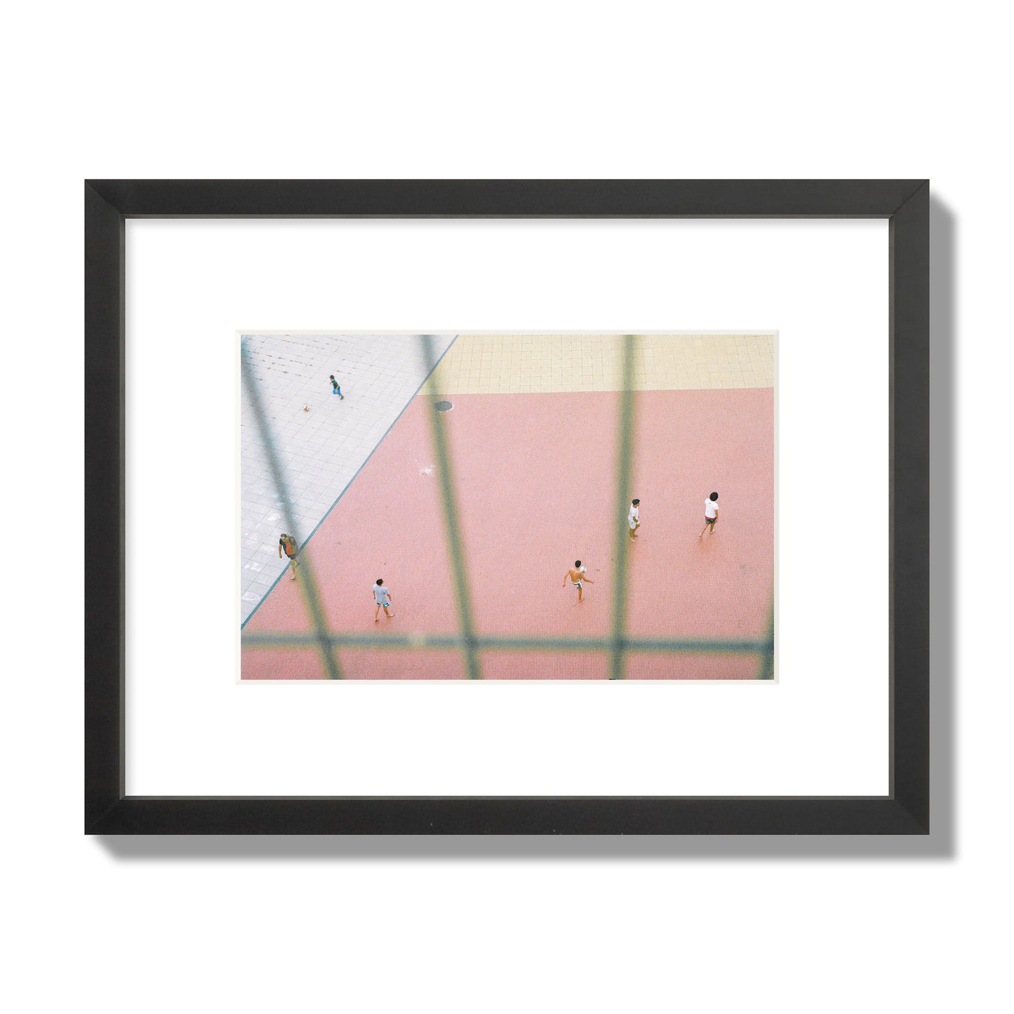 Fine art street photograph of a geometric outdoor scene in Portugal with people playing soccer on a pink field, archival pigment print, small size, black frame.