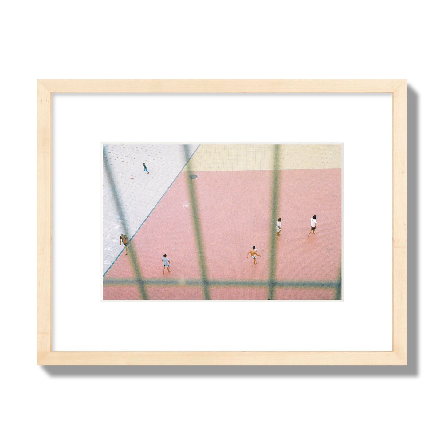 Fine art street photograph of a geometric outdoor scene in Portugal with people playing soccer on a pink field, archival pigment print, small size, natural wood frame.