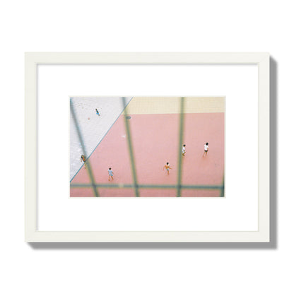 Fine art street photograph of a geometric outdoor scene in Portugal with people playing soccer on a pink field, archival pigment print, small size, white frame.