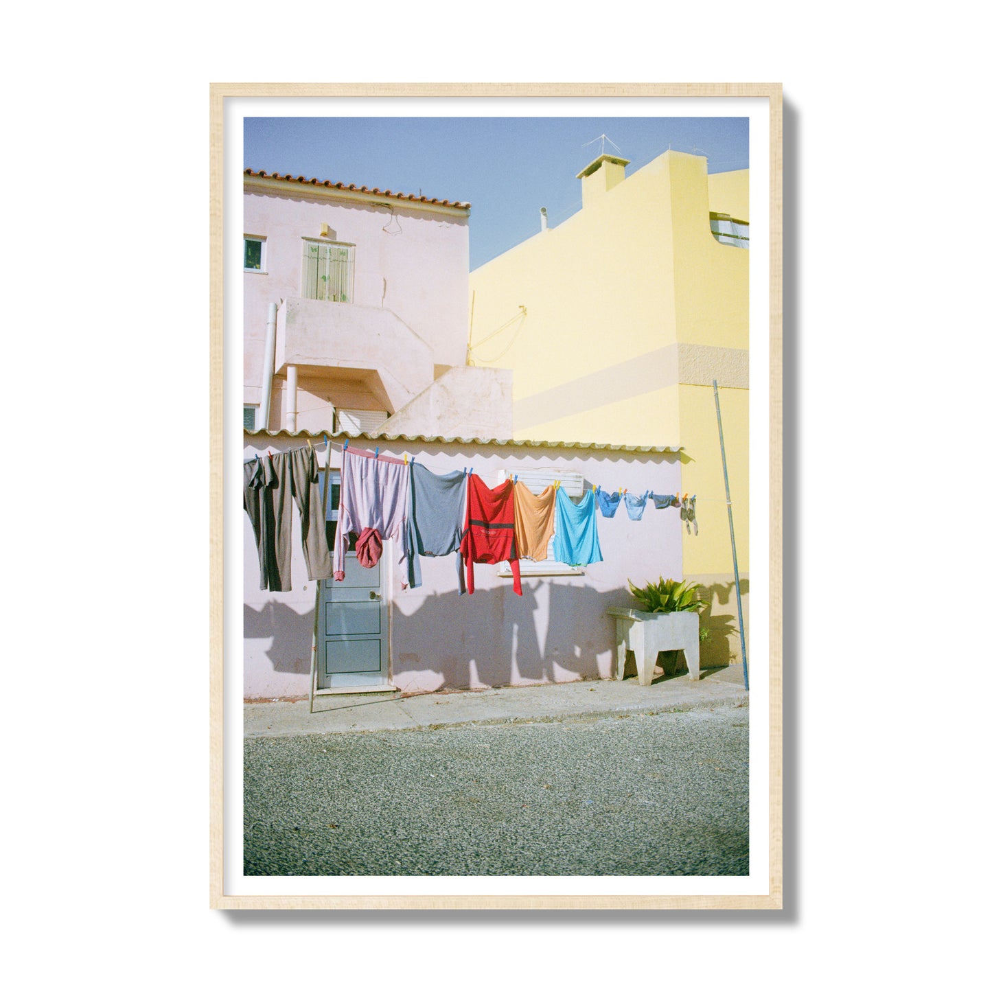 Fine art street photograph of a colorful outdoor scene in Portugal with clothes hanging on a line, archival pigment print, gallery size, natural wood frame.