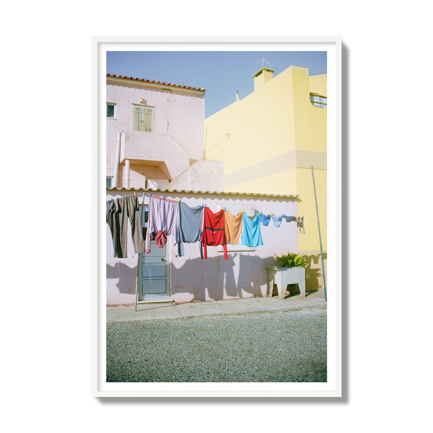 Fine art street photograph of a colorful outdoor scene in Portugal with clothes hanging on a line, archival pigment print, gallery size, white frame.