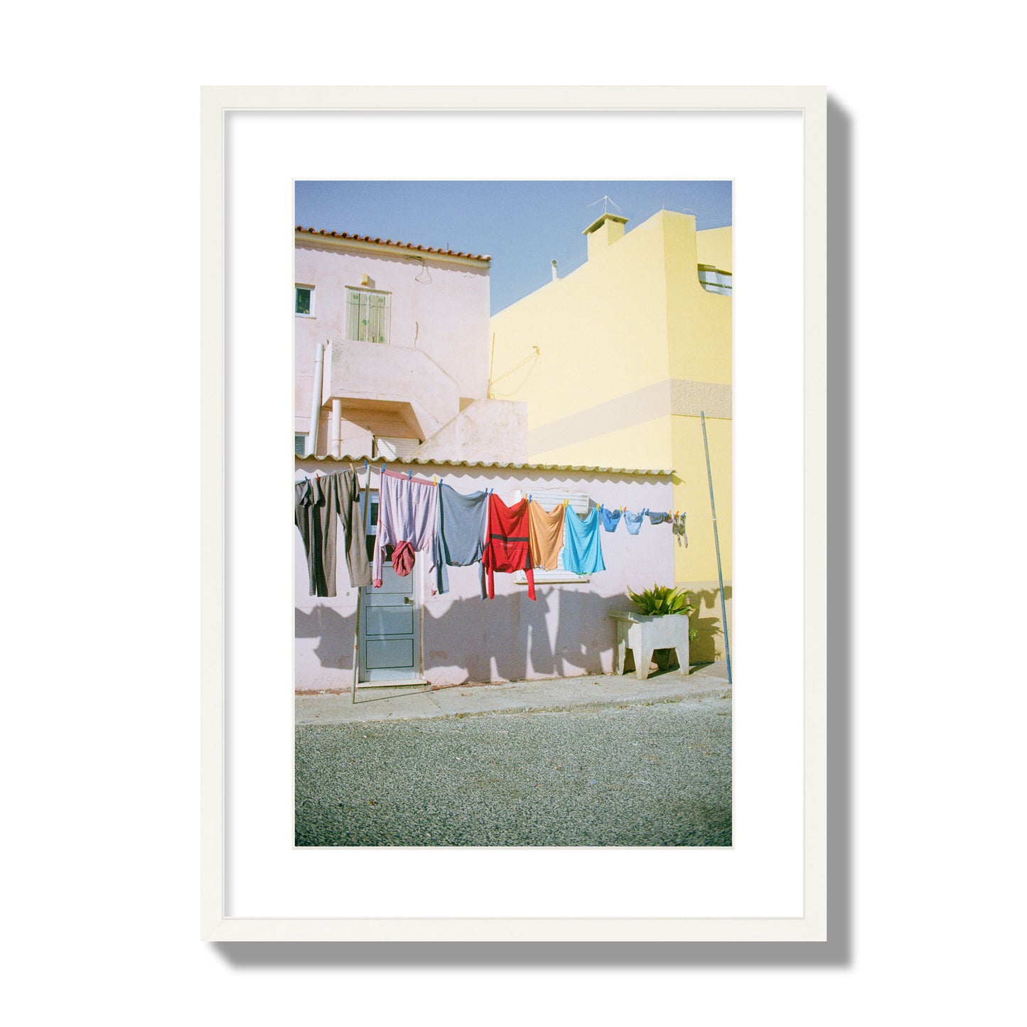 Fine art street photograph of a colorful outdoor scene in Portugal with clothes hanging on a line, archival pigment print, large size, white frame.