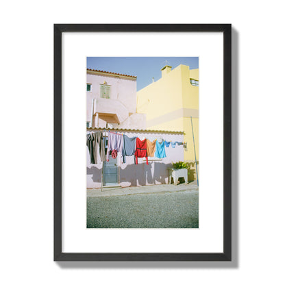 Fine art street photograph of a colorful outdoor scene in Portugal with clothes hanging on a line, archival pigment print, medium size, black frame.