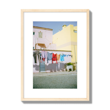 Fine art street photograph of a colorful outdoor scene in Portugal with clothes hanging on a line, archival pigment print, medium size, natural wood frame.