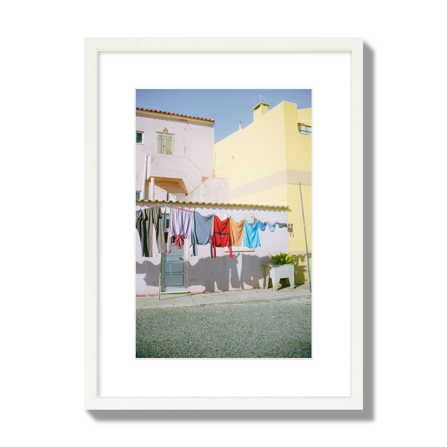 Fine art street photograph of a colorful outdoor scene in Portugal with clothes hanging on a line, archival pigment print, medium size, white frame.