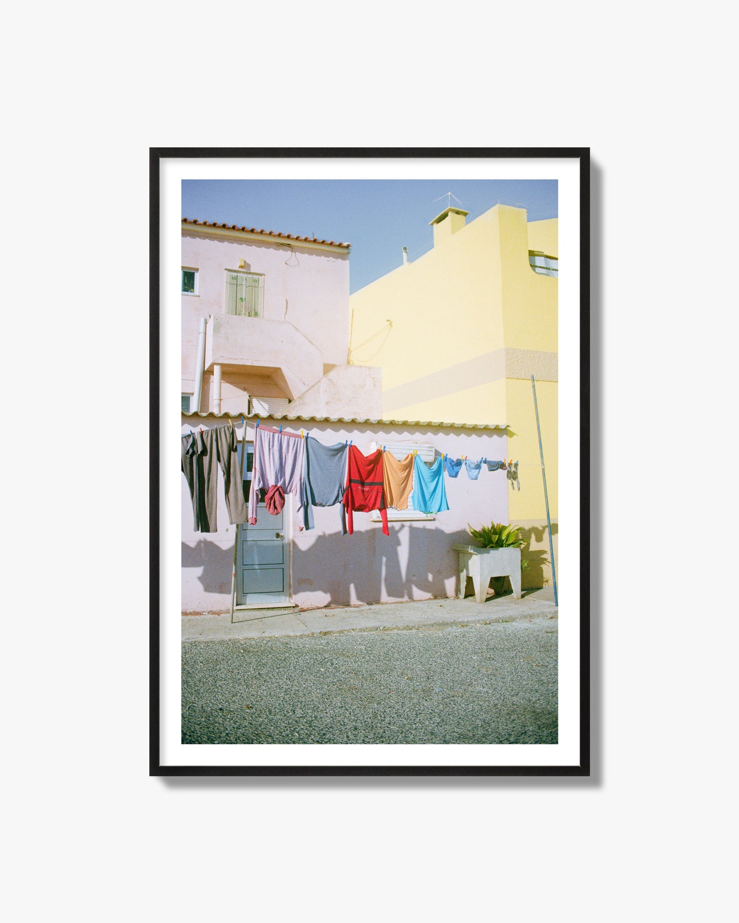 Fine art street photograph of a colorful outdoor scene in Portugal with clothes hanging on a line, archival pigment print in a black frame.
