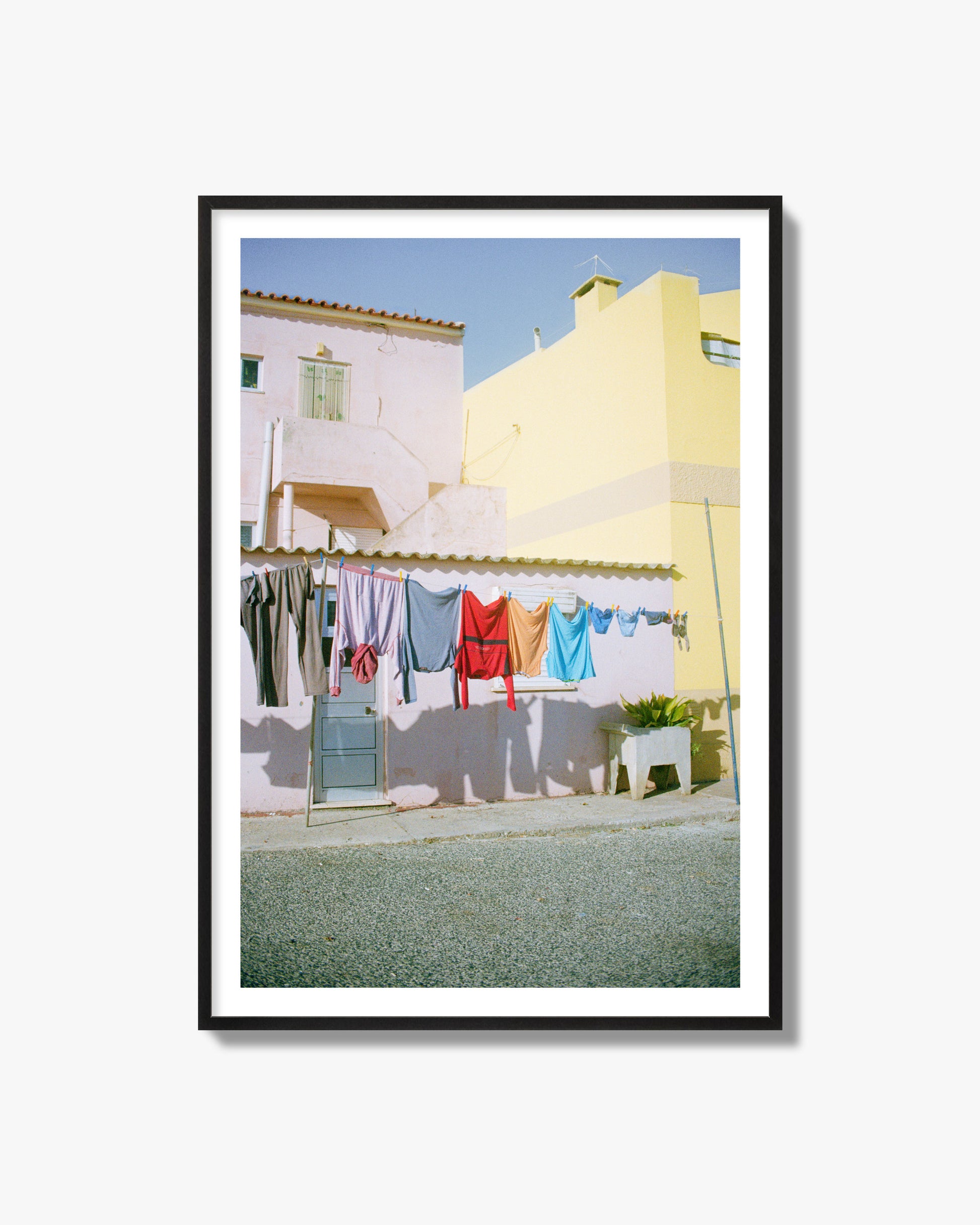 Fine art street photograph of a colorful outdoor scene in Portugal with clothes hanging on a line, archival pigment print in a black frame.
