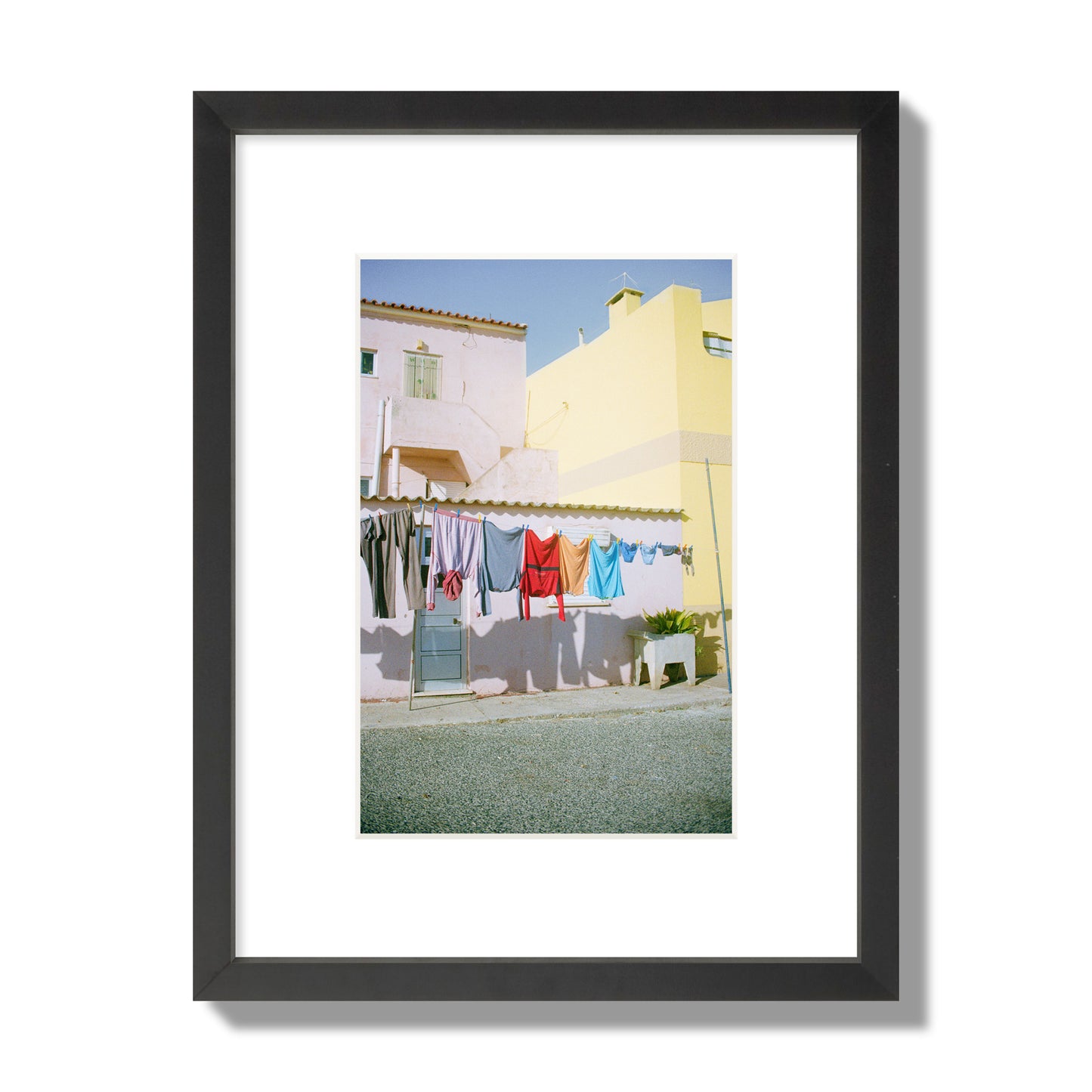 Fine art street photograph of a colorful outdoor scene in Portugal with clothes hanging on a line, archival pigment print, small size, black frame.